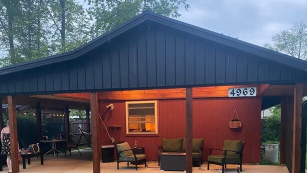 Un espace extérieur abrité avec des tables et des chaises, un panneau indiquant le numéro de l’établissement, du mobilier en bois et une pelouse.