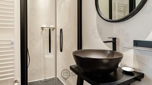 Een moderne badkamer met een grote wastafel, een douchecabine van glas en een ronde spiegel.