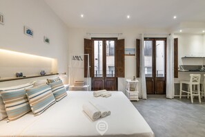 A hotel room with a bed, a desk, and a chair. There are towels on the bed and a shelf with items on the wall. - Studio 73 e 74 - City Centre (Cagliari)