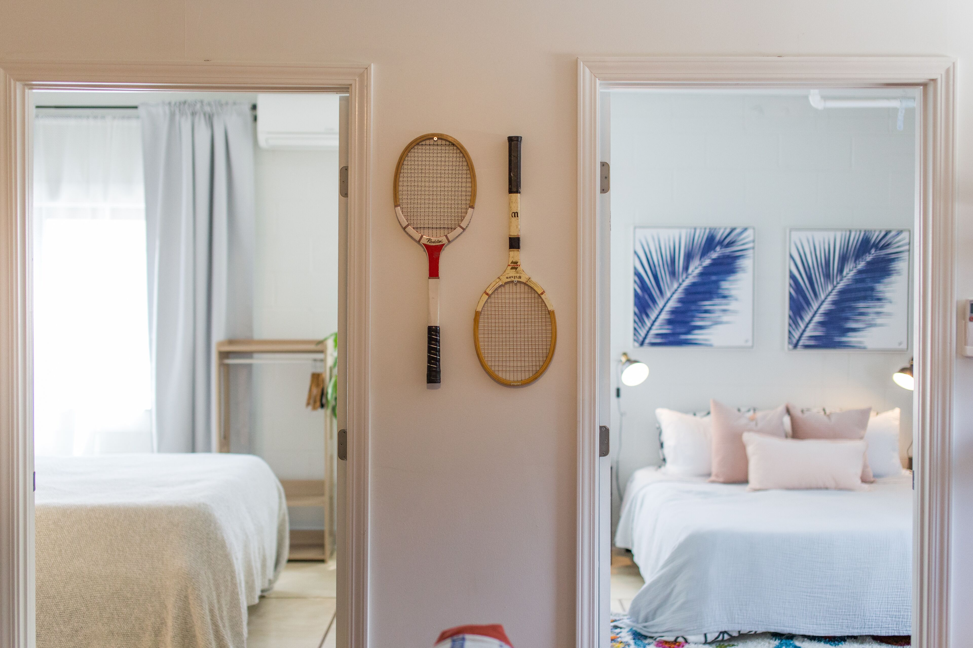 A bedroom with a bed, a wall-mounted rack with two tennis rackets, and two framed wall art pieces.