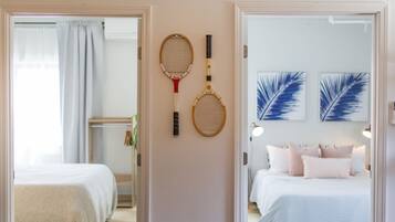 A bedroom with a bed, a wall-mounted rack with two tennis rackets, and two framed wall art pieces.