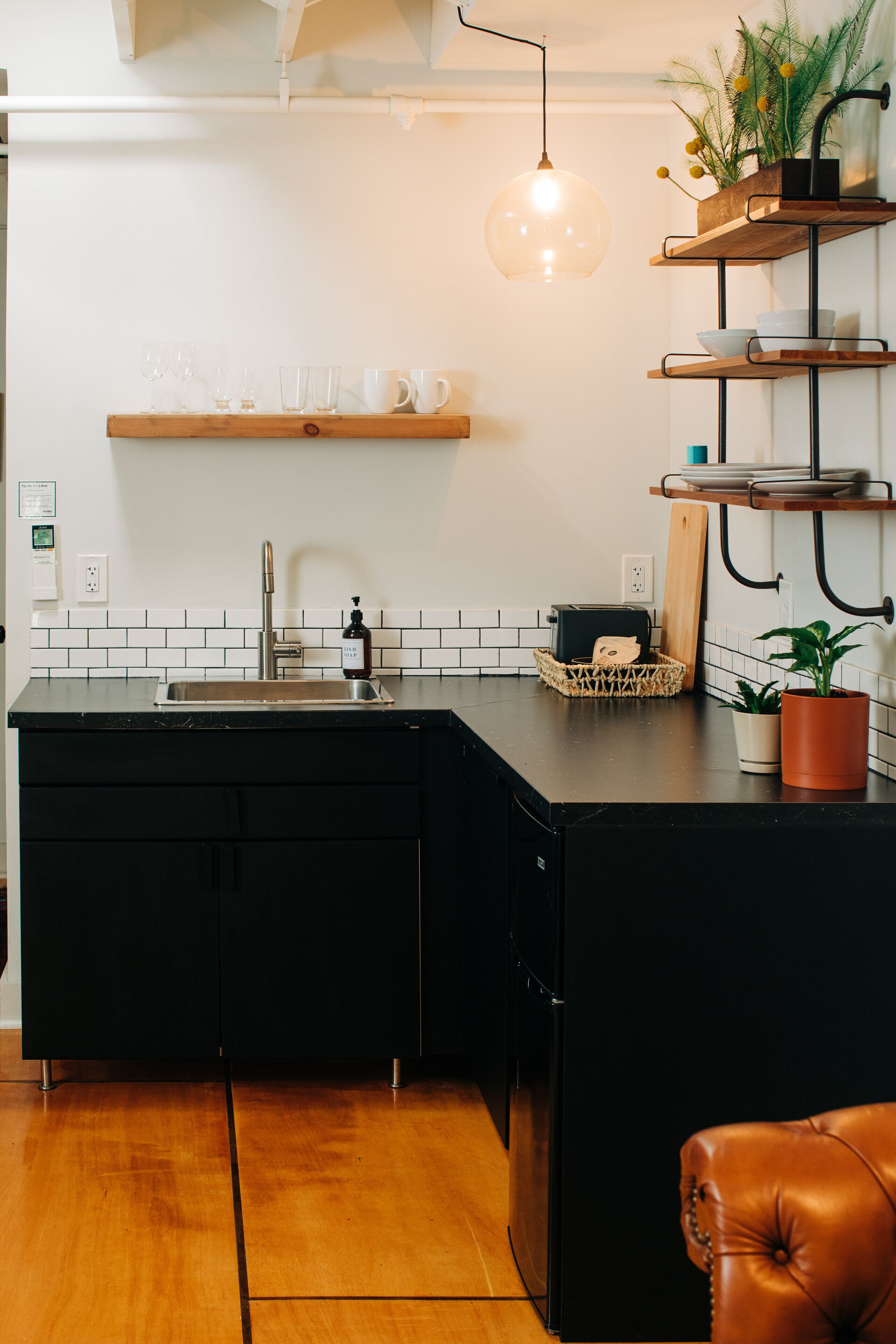 A kitchen with a black countertop, a stainless steel sink, and a wooden island. There are shelves above the countertop holding various kitchen items.