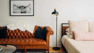 Een kamer met een bruine leren bank, een witte bontmantel, een zwarte vloerlamp en een bed met roze kussens.