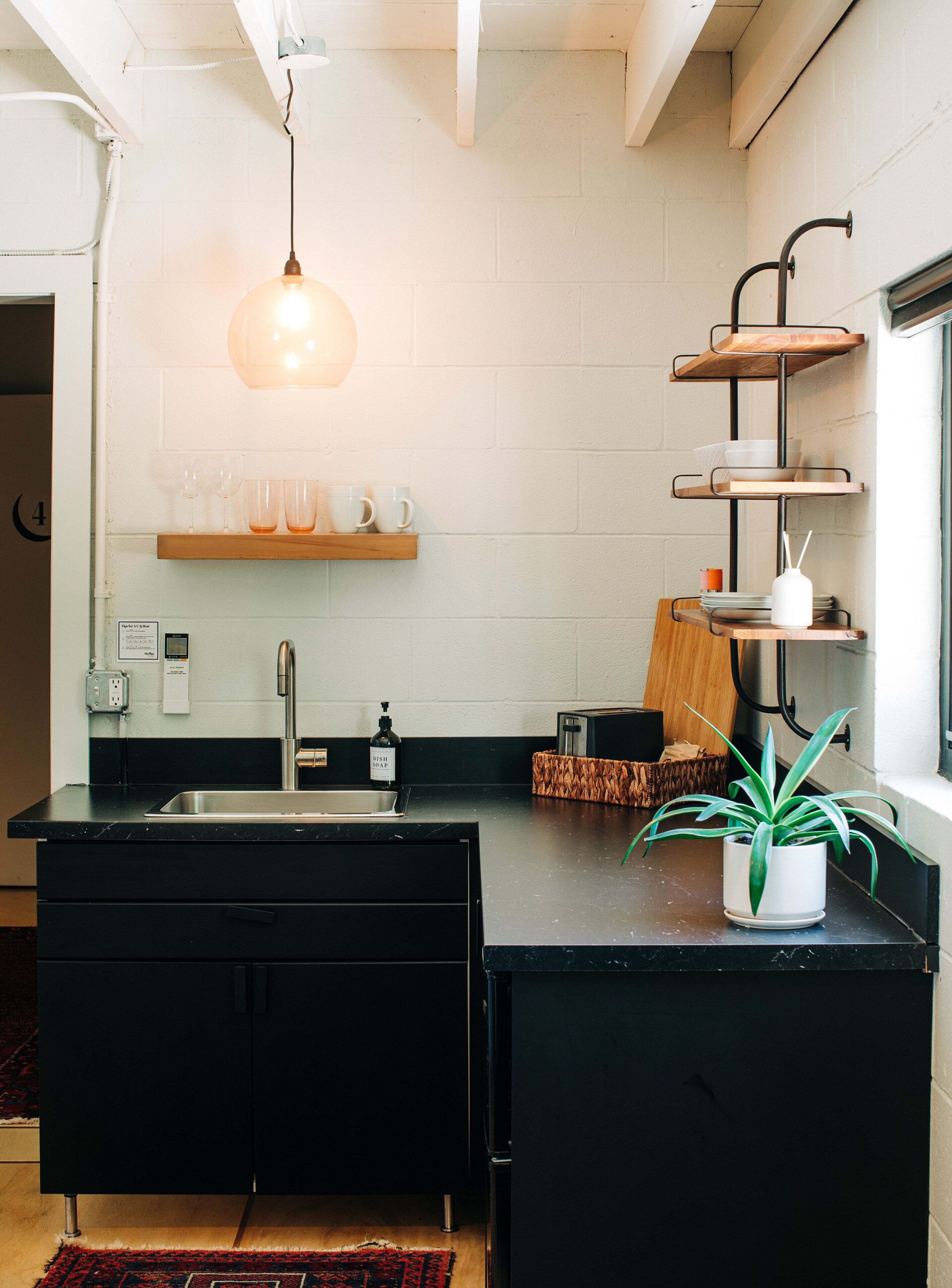 A modern kitchen with a black countertop, a stainless steel sink, a hanging light fixture, and a potted plant.