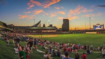 A baseball stadium with a large crowd, a scoreboard, and a tall building in the background.