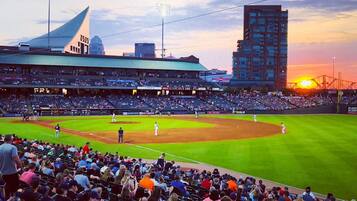 A baseball stadium with a large crowd, a clear sky, and a sunset.