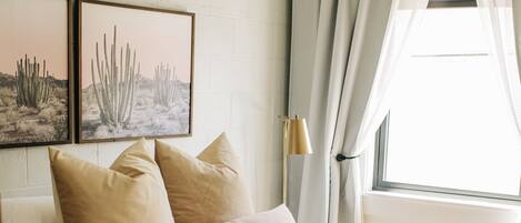 Une chambre à coucher avec un lit, deux tableaux encadrés représentant des paysages désertiques, une lampe de chevet et une fenêtre avec des rideaux.