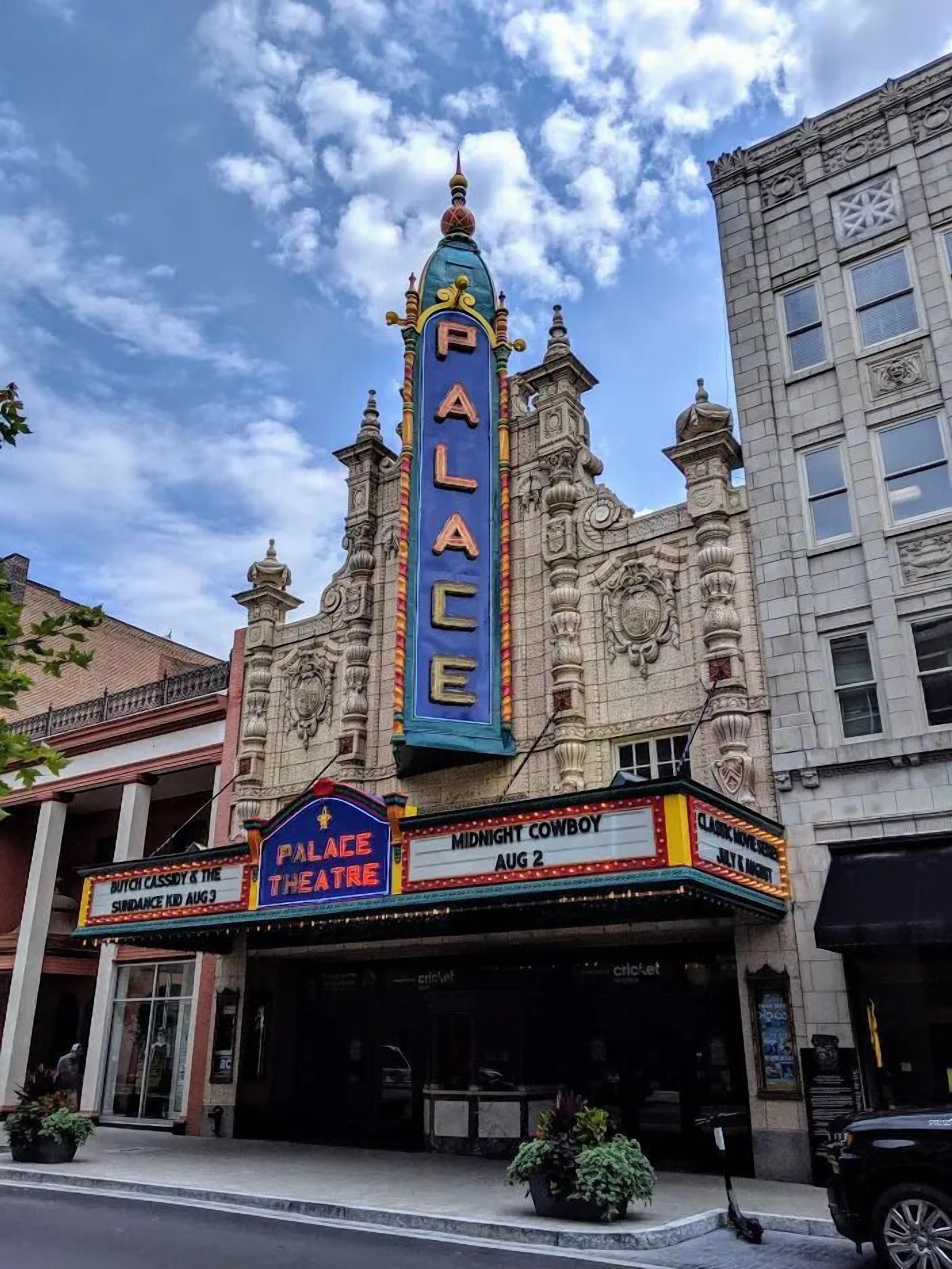 A theater with ornate architecture and a marquee advertising 'Palace Theatre' and 'Midnight Cowboy' showings.