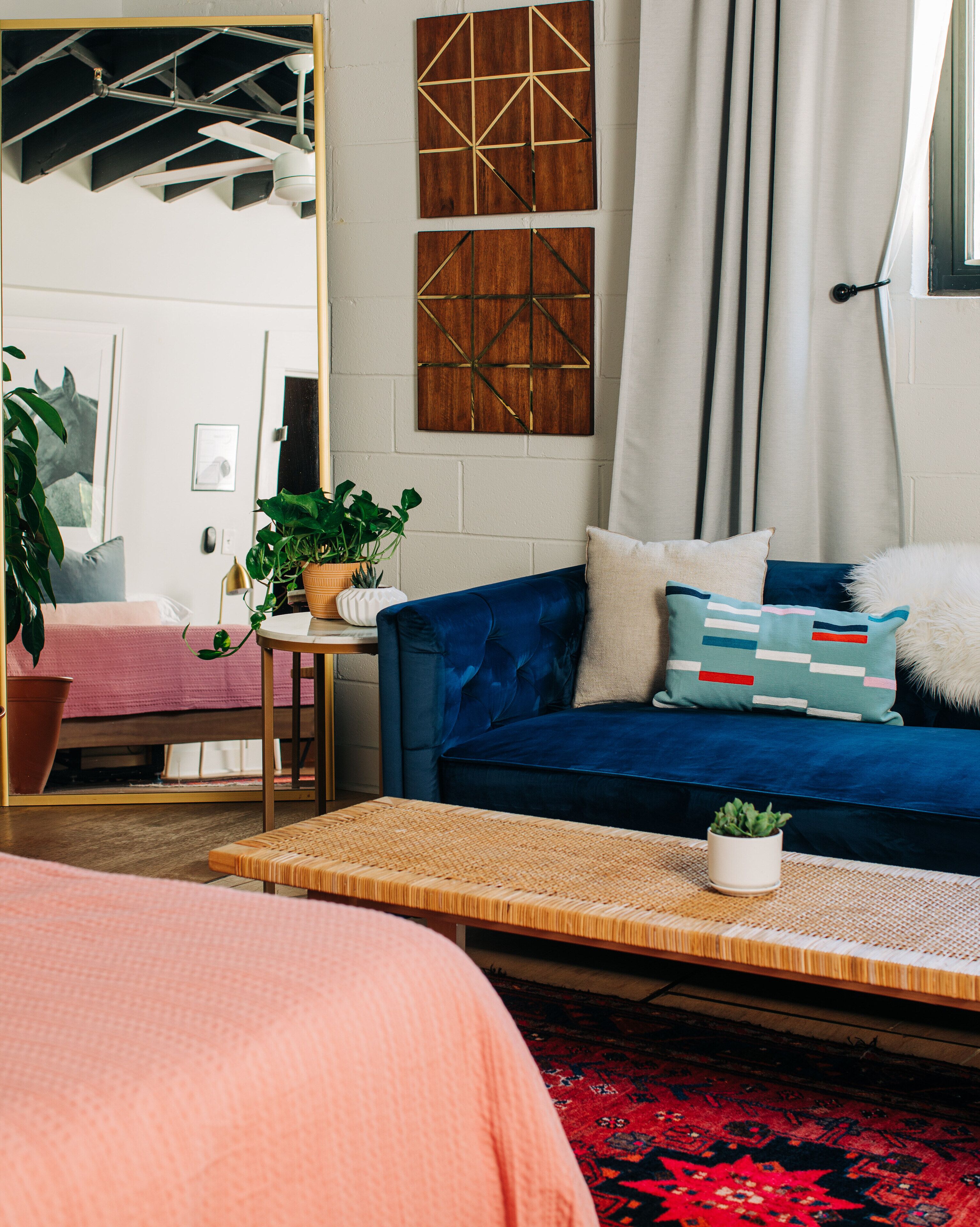 Un salon moderne avec un canapé bleu, une petite table sur laquelle est posée une plante, un grand miroir et un tapis rouge à motifs.