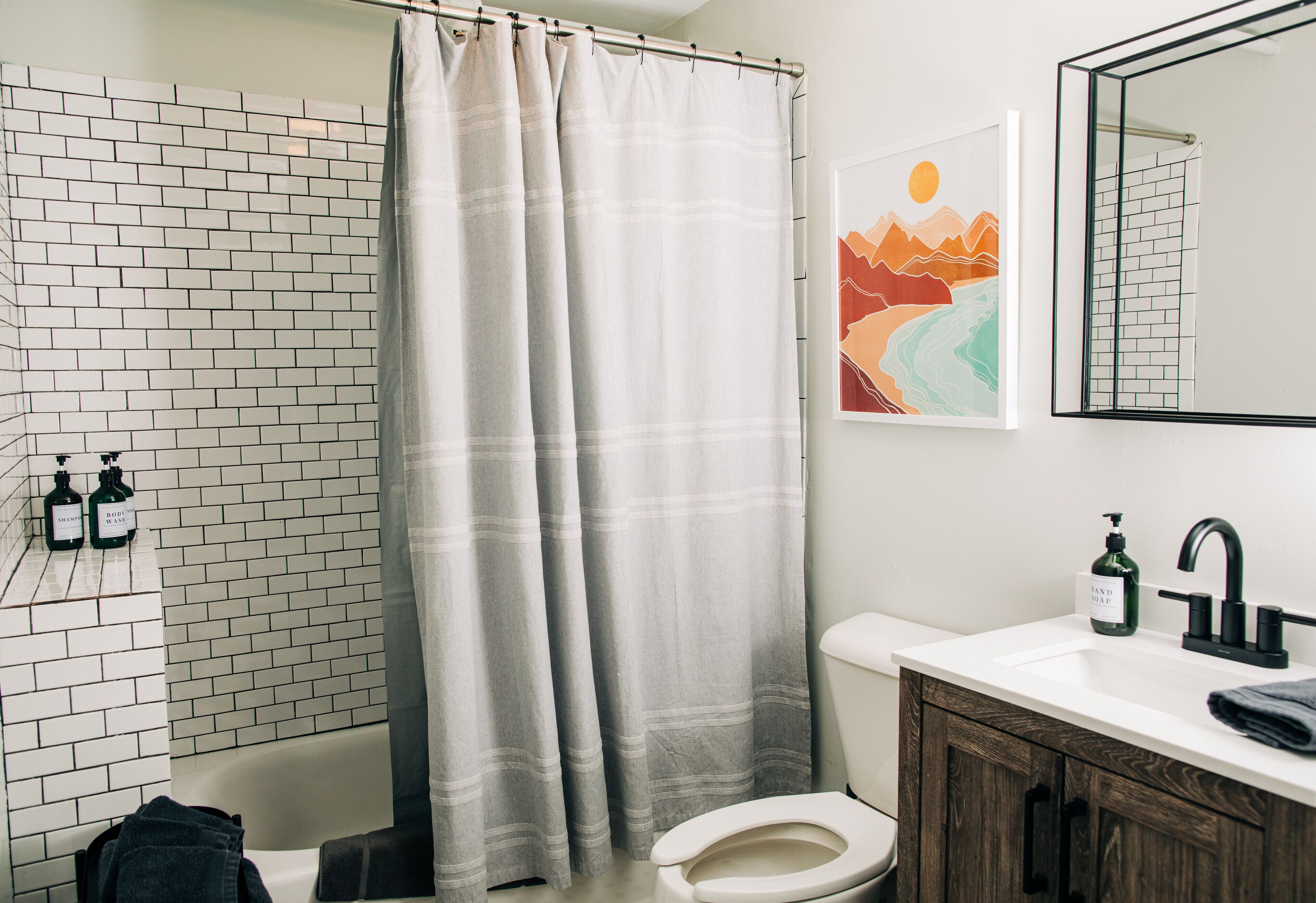 A bathroom with a white bathtub, a shower curtain, a toilet, a sink with a mirror, and a wall-mounted soap dispenser.