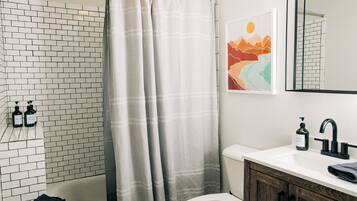 A bathroom with a white bathtub, a shower curtain, a toilet, a sink with a mirror, and a wall-mounted soap dispenser.
