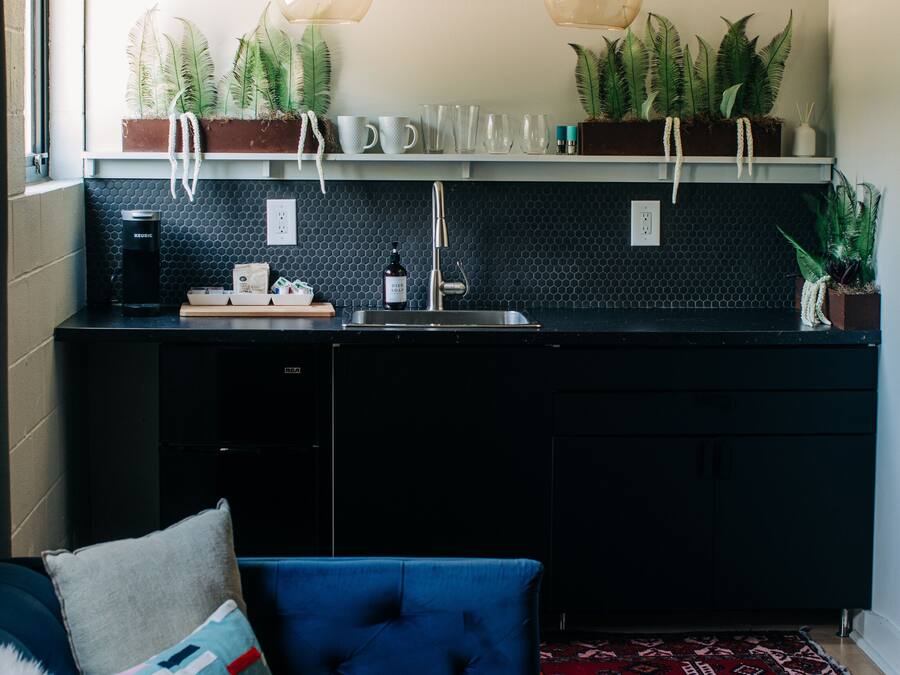A modern kitchen with black cabinets, a black countertop, and a built-in sink. There are two pendant lights, a coffee maker, and a bottle of dish soap on the counter.