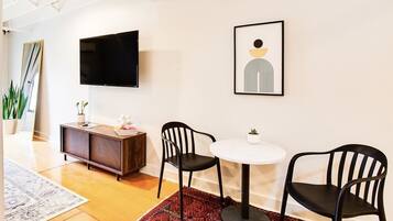 A modern living room with a flat-screen TV, two black chairs, a round white table, and a red patterned rug.
