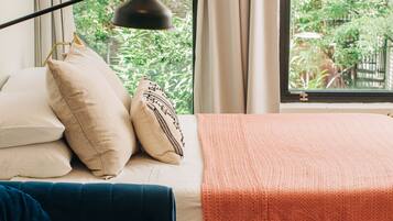 Un dormitorio con cama, un sofá azul, una ventana con cortinas y vistas al exterior.