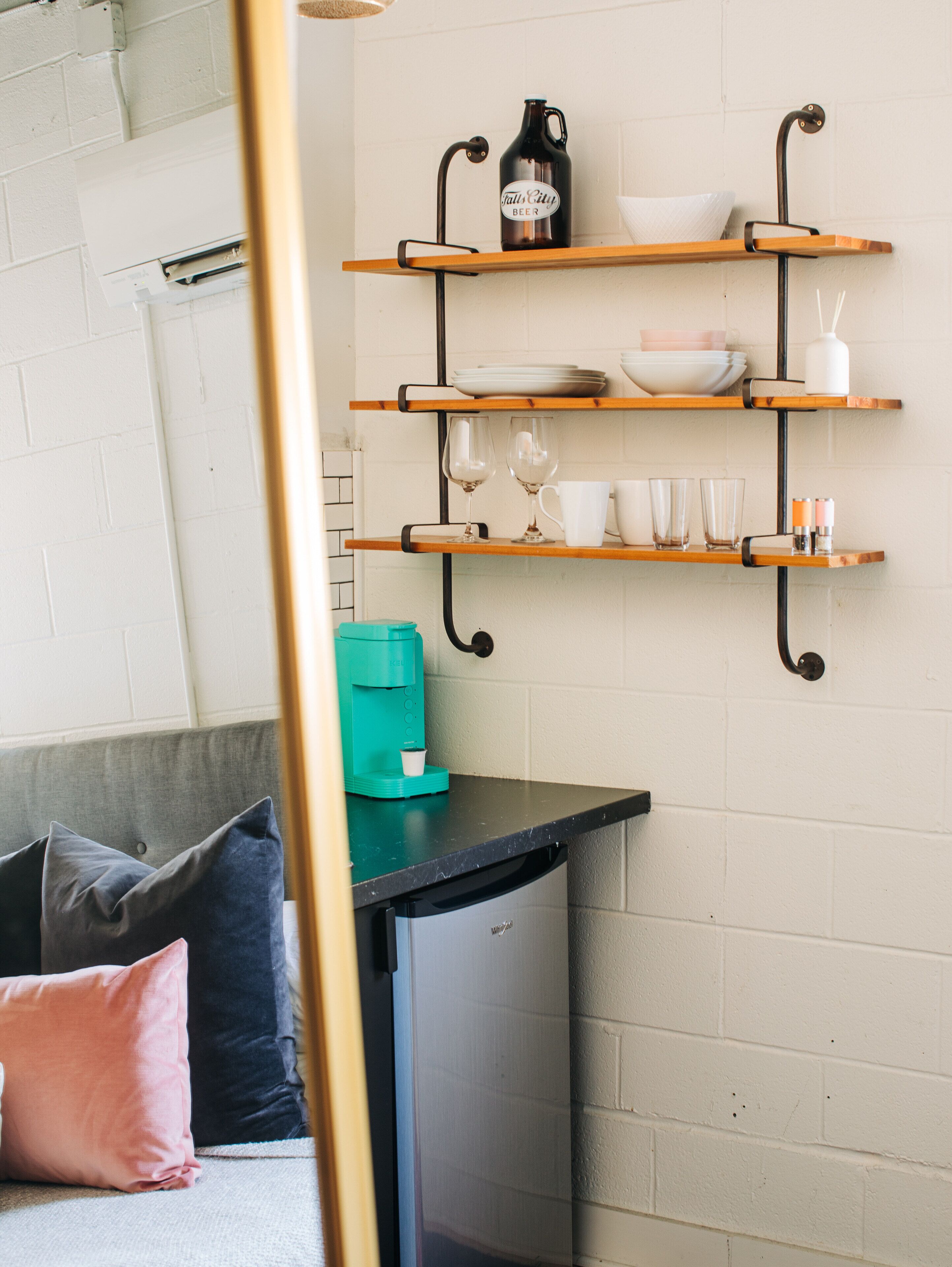 A kitchen with wooden shelves holding dishes, glasses, and a coffee maker.