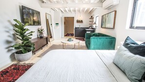 A modern, well-lit room with a large bed, a green sofa, a small round table, and a kitchen area in the background. - Stellar Suites (Louisville)