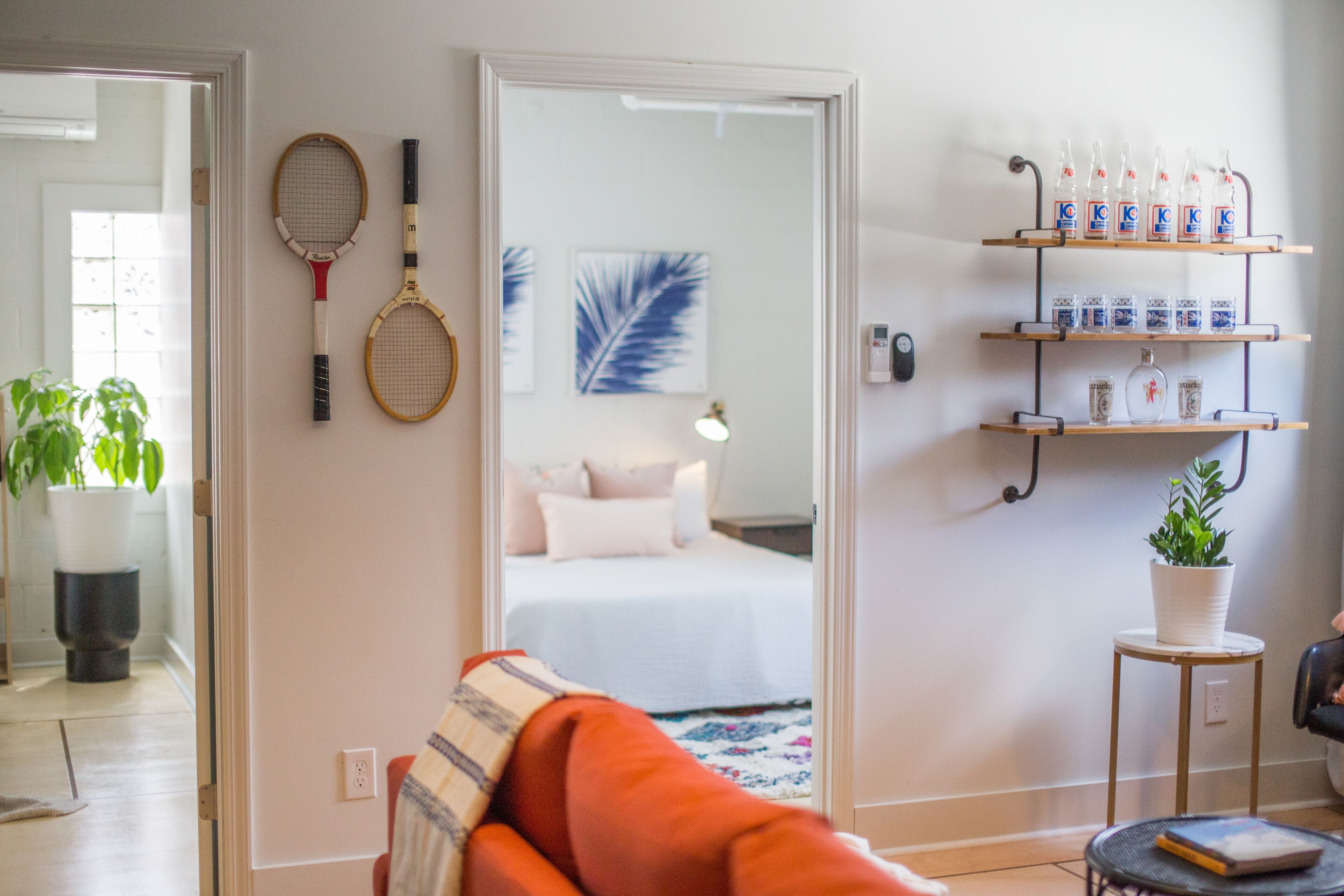 A room with a bed, a mirror, a shelf with bottles, and tennis rackets on the wall.
