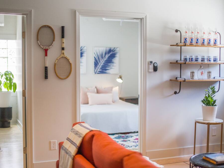 A room with a bed, a mirror, a shelf with bottles, and tennis rackets on the wall.