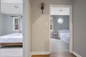 A bedroom with a bed, a window with curtains, a wall-mounted light fixture, and a door leading to another room.