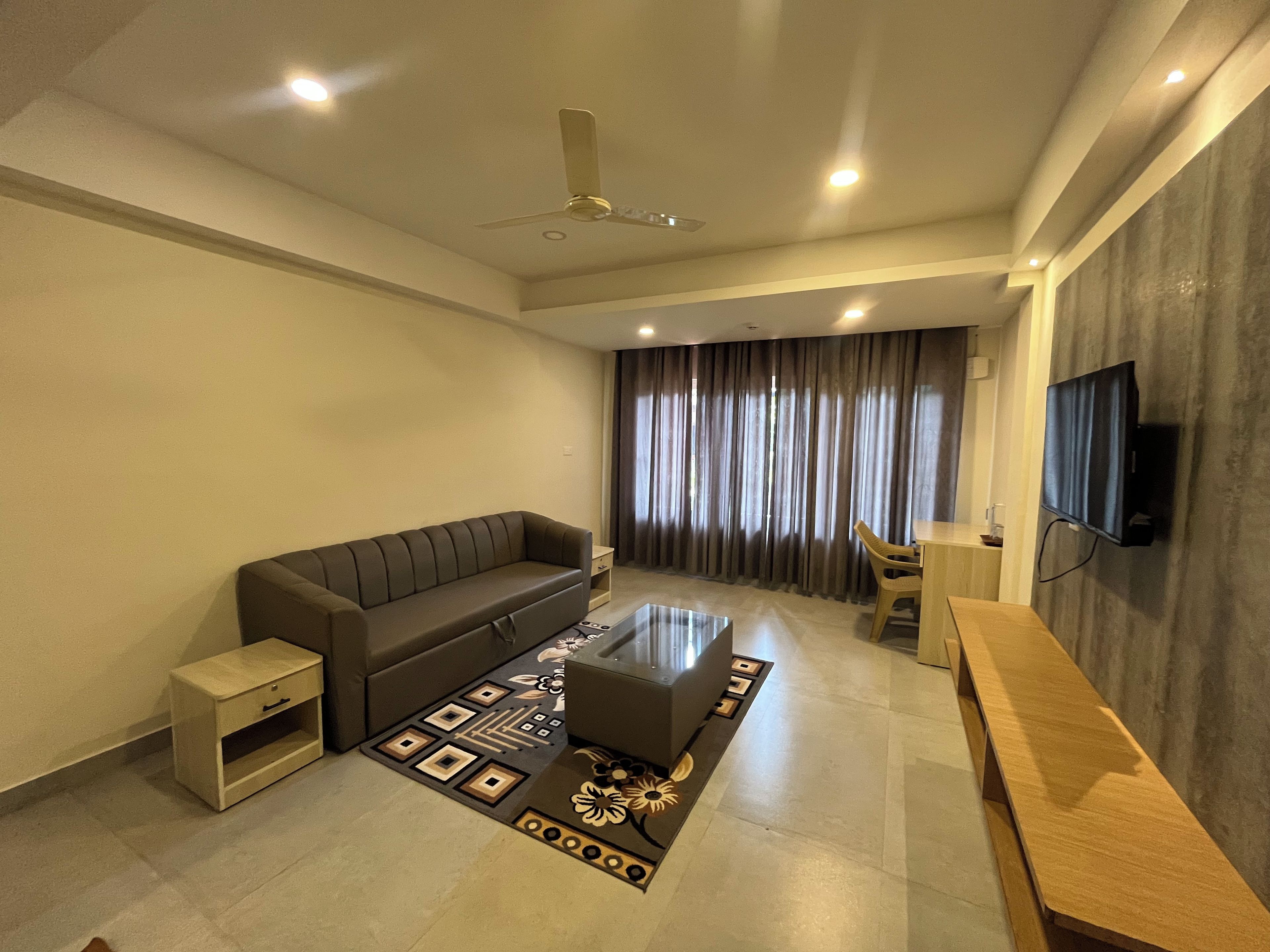A modern living room with a sofa, a coffee table, a TV mounted on the wall, and a ceiling fan.