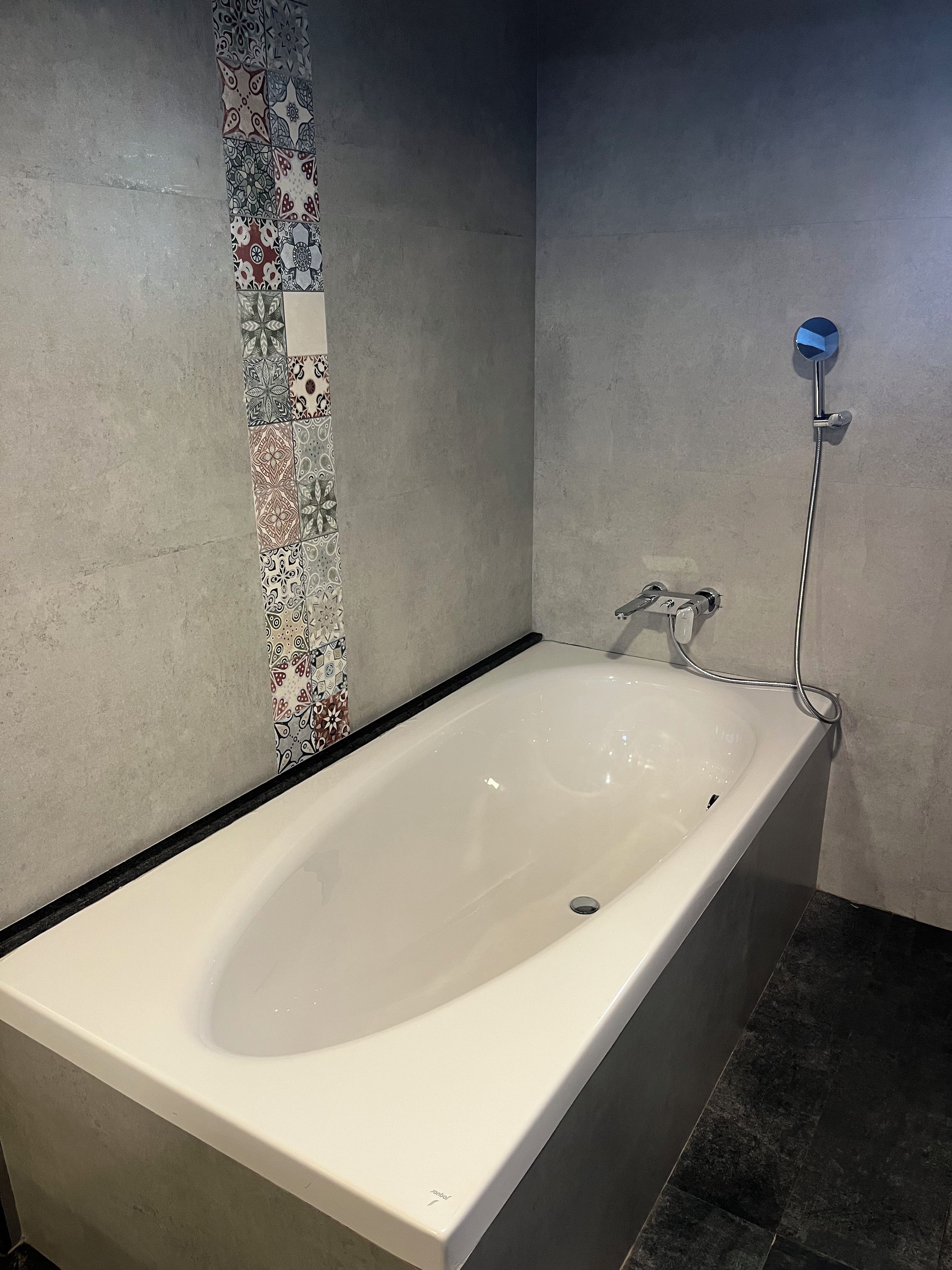 A modern bathroom with a freestanding bathtub, a showerhead, and patterned tiles on the wall.
