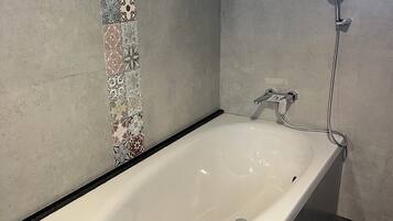 A modern bathroom with a freestanding bathtub, a showerhead, and patterned tiles on the wall.