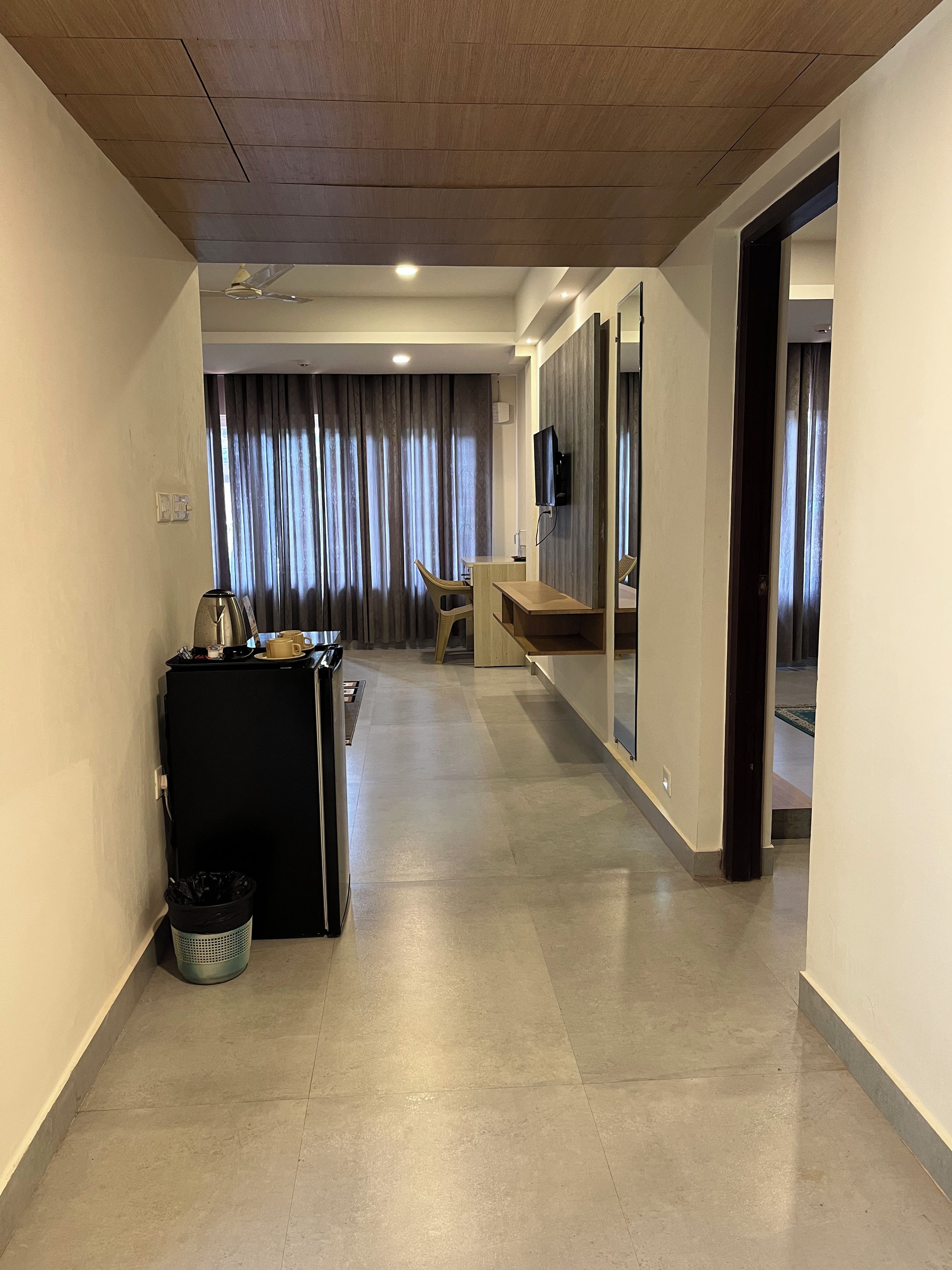 A hotel corridor with a kitchenette, a seating area, and a television.