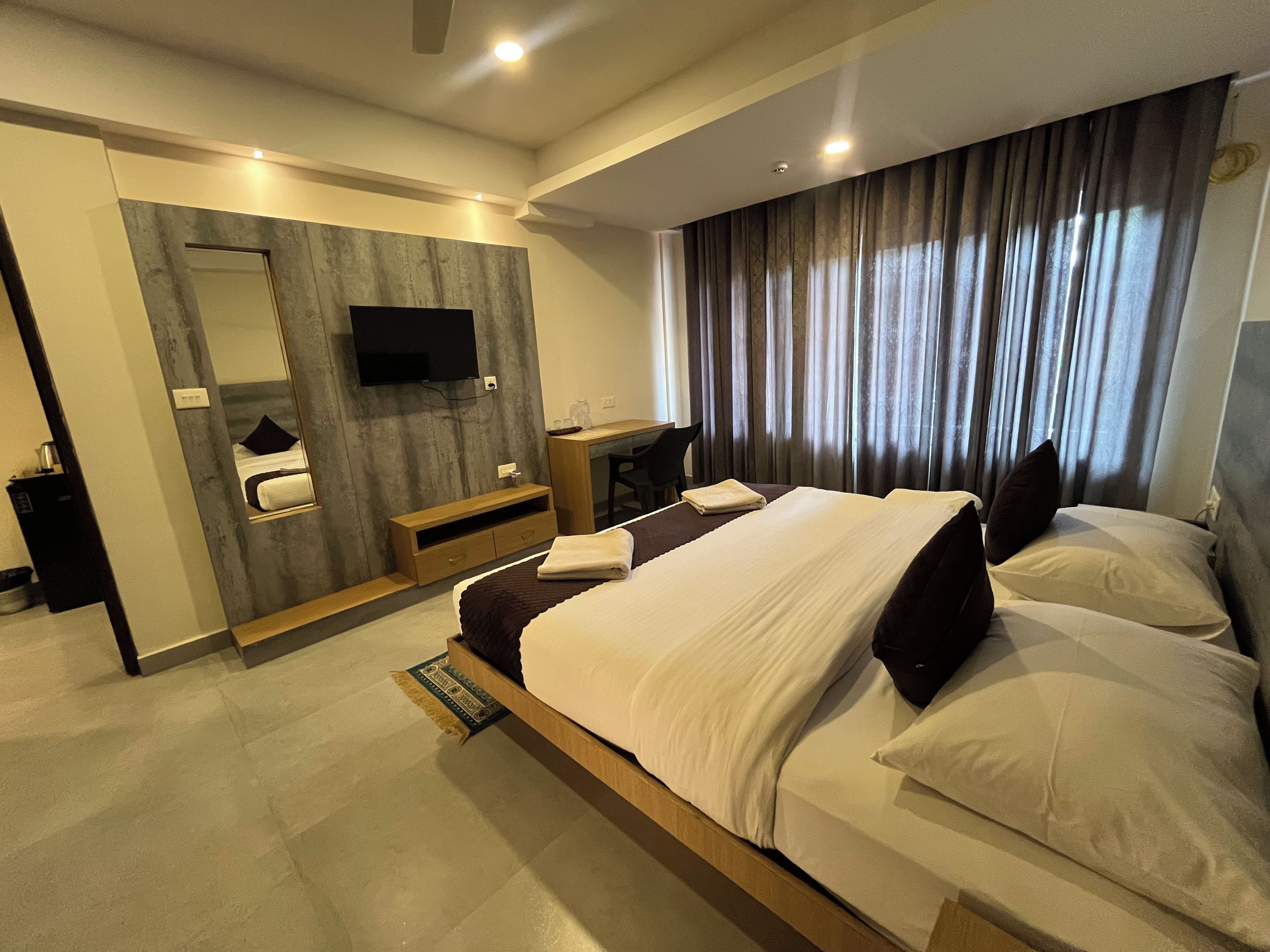 A modern hotel room with a large bed, a desk, a mirror, and a TV.