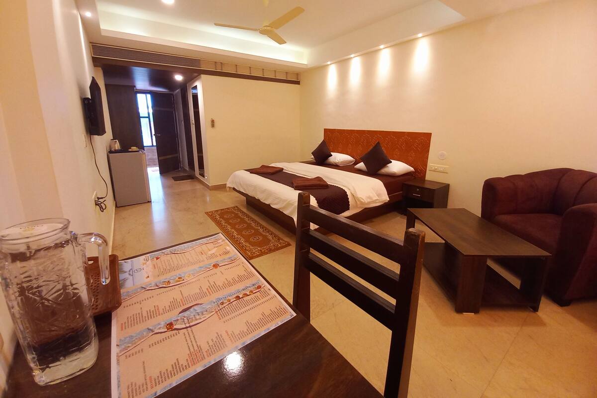 Quarto de hotel com cama, escrivaninha, cadeira, televisão e frigorífico.