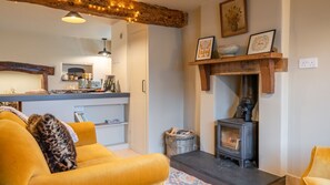 Cozy living room with a black wood-burning stove, wooden shelf, and rustic ceiling with exposed beams.