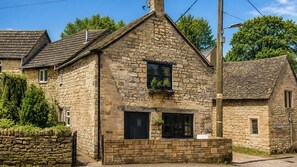 A stone building with a pitched roof, a small window with a plant, and a brick entrance. - Cotswold Way Cottage, Rodborough - sleeps 4 guests  in 2 bedrooms (Rodborough)