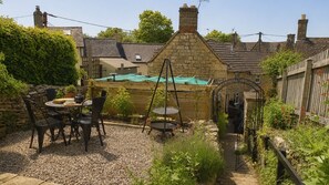 A garden with a stone wall, a swing set, and a table with chairs. - Cotswold Way Cottage, Rodborough - sleeps 4 guests  in 2 bedrooms (Rodborough)