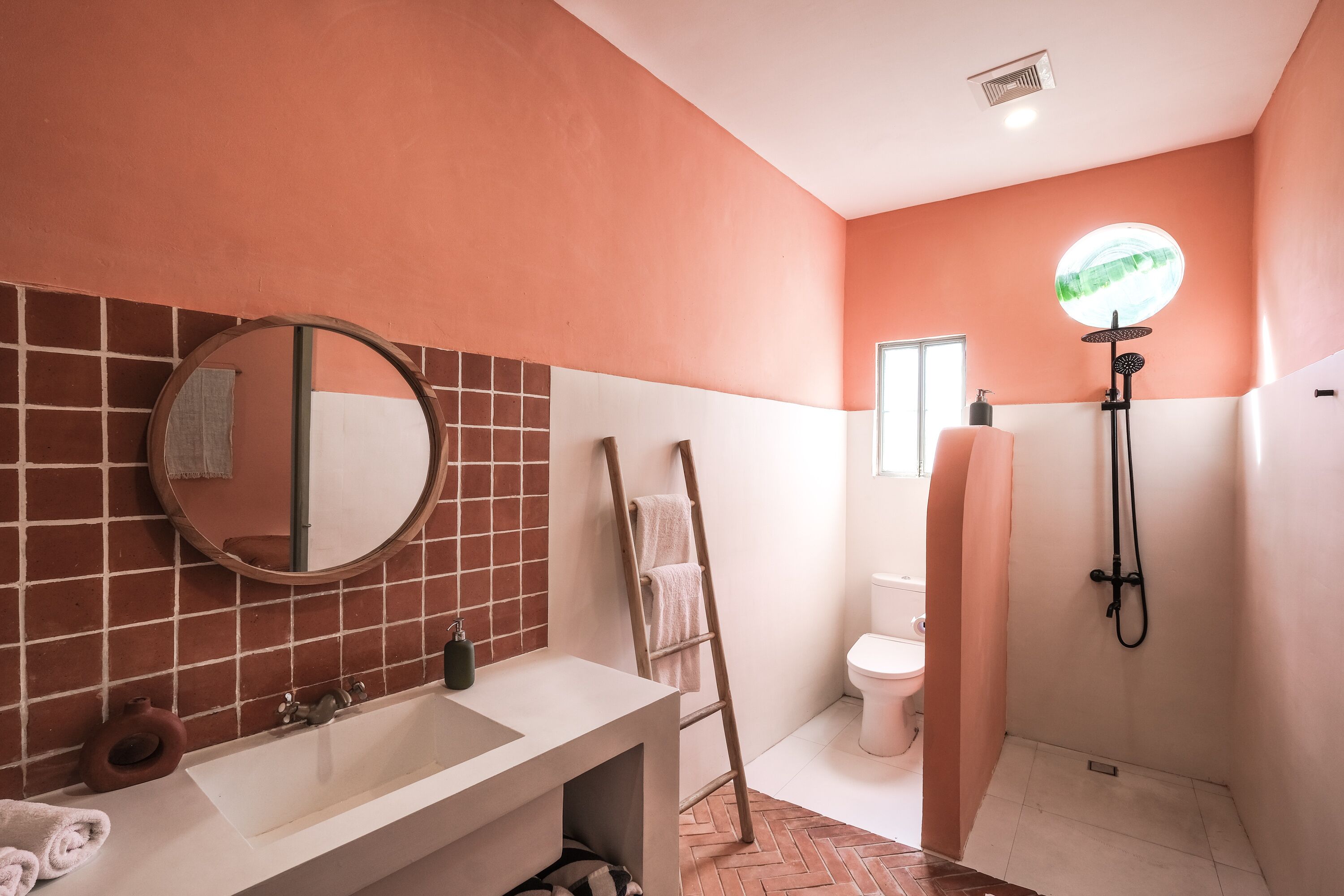A bathroom with a white sink, a round mirror, a towel rack, and a shower area.