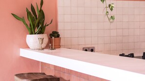 Una cocina con mostrador blanco, tres taburetes de madera, una planta en maceta y salpicadero de azulejos.