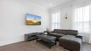 A modern living room with a sectional sofa, a coffee table, and a flat-screen TV mounted on the wall. - Newly constructed 4 Bed luxury house with Private Heated Pool (New Orleans)