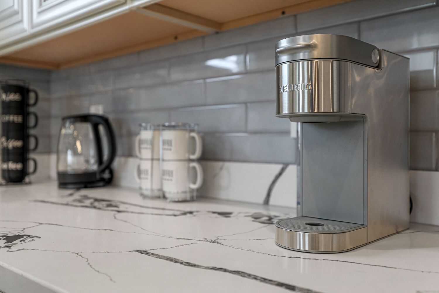 A modern kitchen with a stainless steel Keurig coffee maker on a marble countertop.