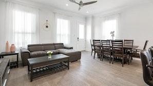 A spacious living room with a sofa, coffee table, dining table with chairs, and a ceiling fan. - Newly constructed 4 Bed luxury house with Private Heated Pool (New Orleans)