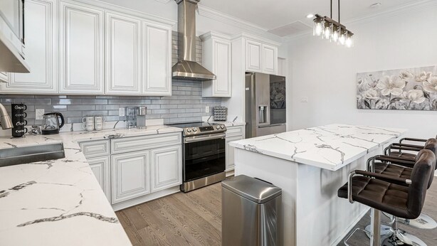A modern kitchen with white cabinetry, a central island, stainless steel appliances, and a bar area with stools. - Newly constructed 4 Bed luxury house with Private Heated Pool (New Orleans)