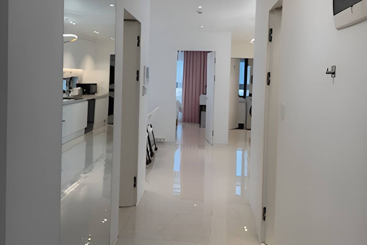 A modern, well-lit hallway with a glossy floor, leading to a room with a large window and a door.