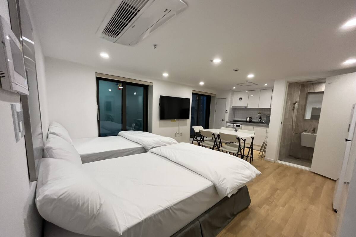A modern hotel room with a large bed, a small kitchenette, and a bathroom.