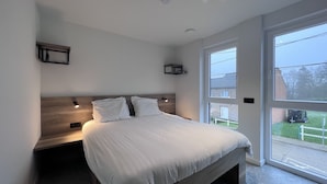 Un dormitorio moderno con una cama grande, cabecera empotrada y vistas al exterior a través de un amplio ventanal.