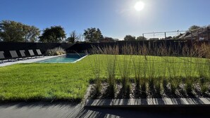 Un patio trasero con piscina, césped y terraza de madera.