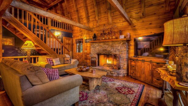 A cozy cabin interior with a stone fireplace, wooden staircase, and rustic decor. - Aska Adventure Cabin on 3 Acres • Hot Tub • Screened Decks • Game Loft (Cherry Log)