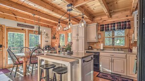 A cozy cabin-style kitchen with wooden beams, a dining area with chairs, and a bar with stools. - Aska Adventure Cabin on 3 Acres • Hot Tub • Screened Decks • Game Loft (Cherry Log)
