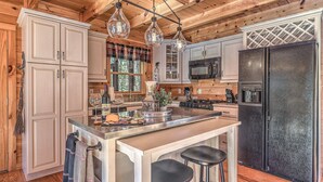 A kitchen with wooden cabinets, a central island with stools, a refrigerator, and hanging pendant lights. - Aska Adventure Cabin on 3 Acres • Hot Tub • Screened Decks • Game Loft (Cherry Log)
