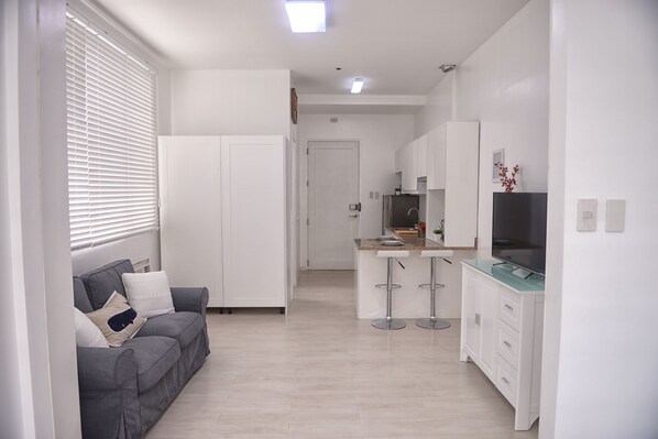 Una cocina moderna con armarios blancos, una isla central con taburetes y un sofá gris con cojines.