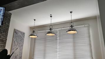 Una habitación con pared de ladrillo, un ventanal con persianas y tres lámparas colgantes.