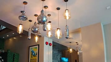 A hotel lobby with multiple hanging pendant lights, a framed poster on the wall, and a television screen.