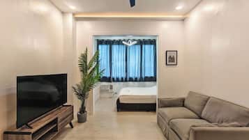 A modern hotel room with a flat-screen TV, a sofa, a potted plant, and a bed with a window view.