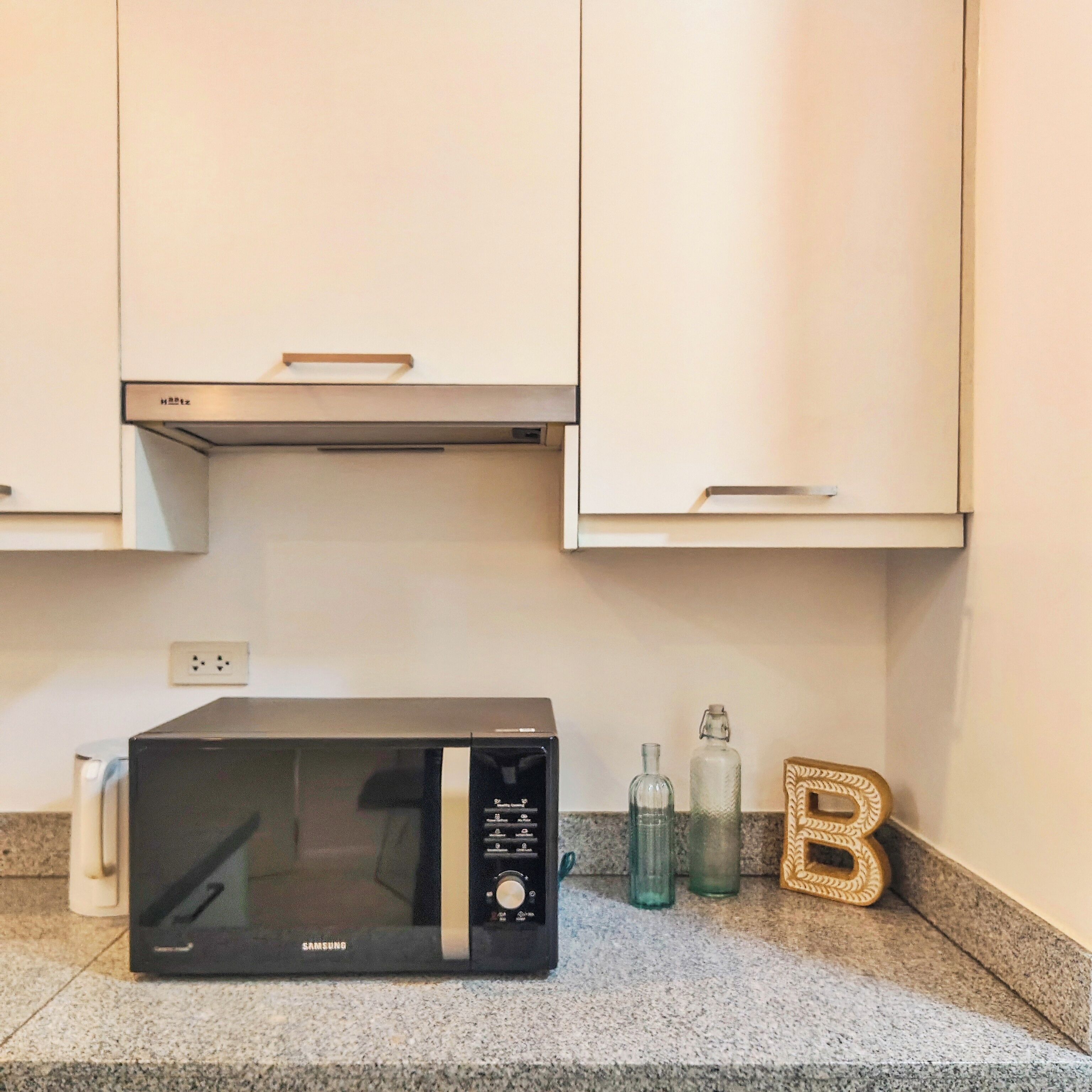 Cozinha com micro-ondas preto, armários brancos e bancada de granito.